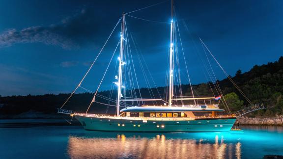 The Son de Mar stands brightly lit at night on the still water in a bay.